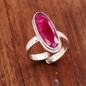 May include: A silver ring with a large, oval-shaped ruby gemstone. The ruby is a deep red color and has a faceted cut.