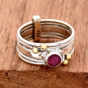 K&ouml;nnte beinhalten: Ein silberner Ring mit einem roten Edelstein und goldenen Akzenten. Der Ring besteht aus mehreren B&auml;ndern und hat eine Gr&ouml;&szlig;e 9, die auf der Seite eingepr&auml;gt ist.