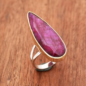 Peut inclure: Une bague en forme de larme avec une grande pierre précieuse rose facetée sertie dans une bélière en or. La bande de la bague est en argent et a une tige fendue.