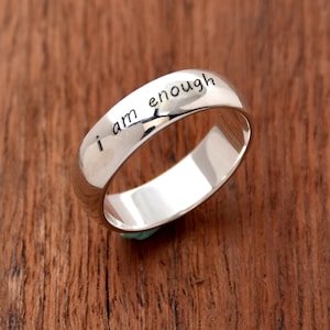 May include: A silver band ring with the words "i am enough" engraved on the outside of the band.