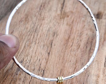 May include: A silver bangle bracelet with a hammered texture and three gold rings attached to the side.