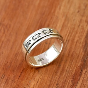 May include: A silver spinning ring with a design of bears walking around the band. The ring is engraved with the number "925" on the inside.