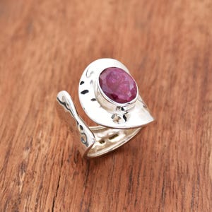 Puede incluir: Un anillo de plata con acabado martillado y una gran piedra preciosa de rubí de forma ovalada engastada en un engaste de bisel.