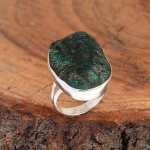 Puede incluir: Un anillo de plata con una gran piedra preciosa verde de forma irregular. El anillo está engastado en una banda simple de plata.