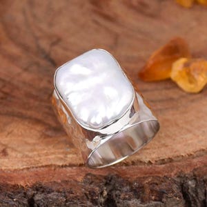 Puede incluir: Un anillo de plata con una perla grande, blanca e irregular, engastada en una banda texturizada.