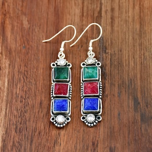 May include: Silver-toned earrings with a rectangular design. Each earring features three square gemstones in green, red, and blue, with a small clear stone at the top and bottom. The earrings hang from a curved hook.