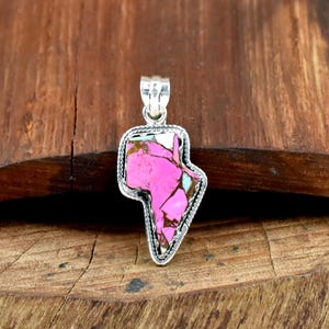 May include: A silver pendant with a pink, white, and turquoise stone in a unique shape. The stone is set in a silver frame with a rope-like border. The pendant hangs from a silver bail.