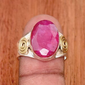 Könnte beinhalten: Ein silberner Ring mit einem großen ovalen rosafarbenen Rubin. Der Ring hat zwei goldene Akzente auf beiden Seiten des Steins.