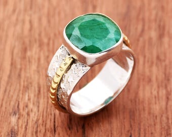 May include: A silver ring with a green emerald gemstone set in a gold bezel. The band is textured and has a gold accent.