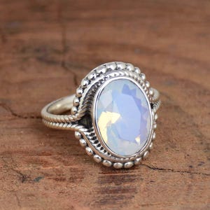 May include: A silver ring with a large oval-shaped opal gemstone. The ring has a beaded design around the stone and a twisted band.