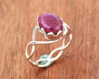 Puede incluir: Un anillo de plata con una gran piedra preciosa de rubí de forma ovalada. El anillo tiene una banda delicada y retorcida.