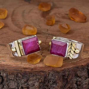 Op de afbeelding: Twee zilveren ringen met gouden accenten en rode edelsteen bezettingen. De ringen hebben een vierkante edelsteen met een facetgeslepen ontwerp.