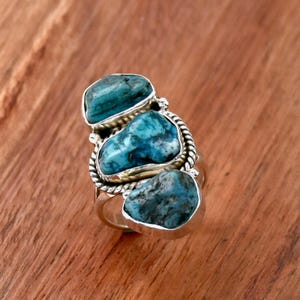 May include: A silver ring with three turquoise stones set in a twisted silver band.