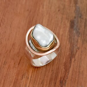 May include: A silver ring with a gold band and a large white pearl set in the center.