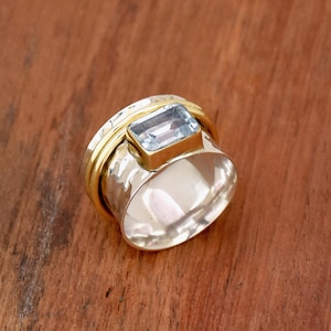 May include: A silver and gold spinning ring with a light blue rectangular gemstone.
