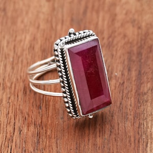 May include: A silver ring with a large, rectangular, deep red ruby gemstone set in a detailed silver bezel. The ring has a double band.