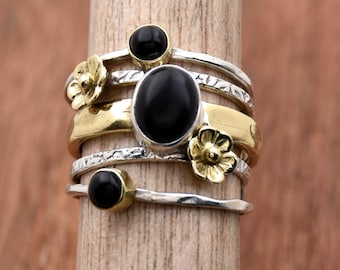 May include: A silver and gold ring with black gemstones and flower accents. The ring is stacked with multiple bands.
