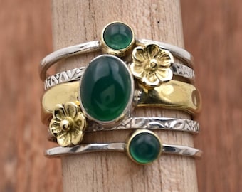 May include: A silver and gold ring set with five green gemstones and three gold flower accents.