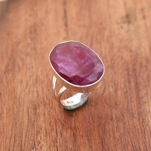 May include: A silver ring featuring a large, oval-shaped, deep pink ruby gemstone. The ring has a simple, elegant design.