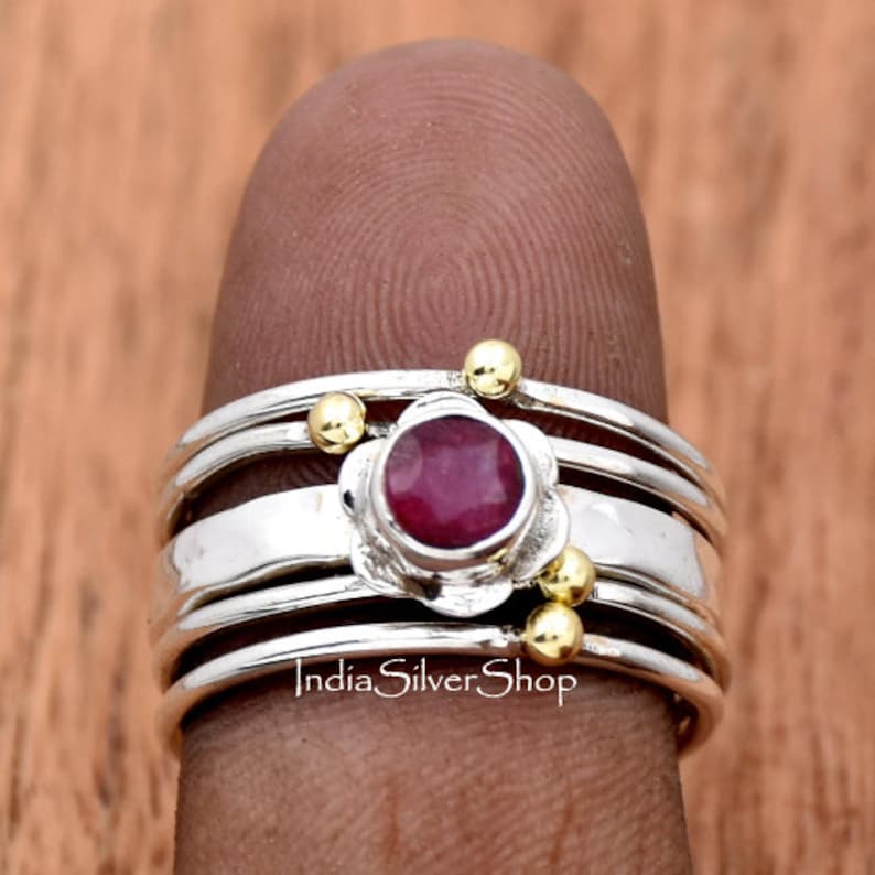 K&ouml;nnte beinhalten: Ein Silberring mit vier B&auml;ndern und einem roten Edelstein, der in einem Blumenmuster gefasst ist. Der Ring ist mit kleinen goldenen Perlen verziert.