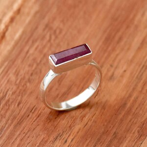 以下が含まれることがあります： シンプルなバンドに、長方形のルビーの宝石がセットされたシルバーリングです。