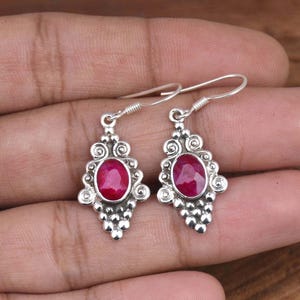 Puede incluir: Un par de pendientes de plata con una piedra preciosa ovalada rosa engastada en un diseño de plata detallado. Los pendientes tienen un cierre de gancho.