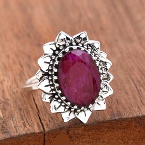 May include: A silver ring featuring a large, oval-shaped, deep pink gemstone set within a floral design.
