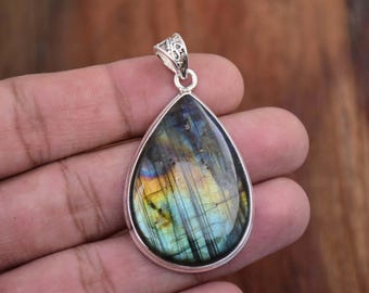 May include: A teardrop-shaped pendant with a silver setting and a large iridescent labradorite gemstone. The gemstone has a blue, green, and gold color.