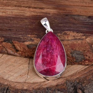 May include: A teardrop-shaped pendant featuring a deep red ruby gemstone set in sterling silver.