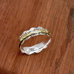 Puede incluir: Un anillo de plata y oro con un diseño texturizado. El anillo está marcado con el número "925" en el interior.