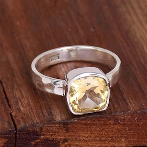 May include: A silver ring with a large, square-shaped, yellow gemstone. The ring has a hammered texture.