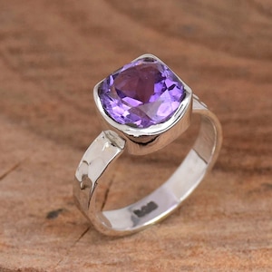 May include: A silver ring featuring a large, square-shaped amethyst gemstone. The ring band is hammered and has a textured finish.