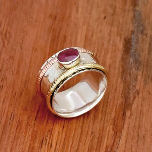 May include: A silver ring with a red gemstone set in a gold band. The ring has a textured silver band with a copper band underneath.