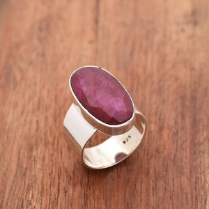 Könnte beinhalten: Ein silberner Ring mit einem großen ovalen Rubin-Edelstein. Der Ring ist in einer schlichten Bandfassung gefasst und trägt die Punze 925.