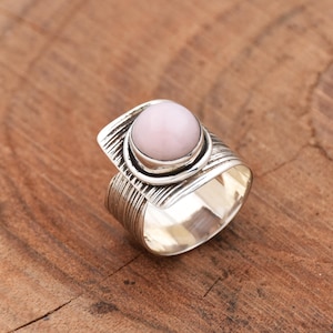 May include: A silver ring with a textured band and a round pink opal gemstone.