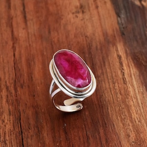 May include: A silver ring with a large, oval ruby gemstone. The ruby is a deep red colour, set in a double-banded silver frame. The ring's band has an open design, and the gemstone is the focal point of the ring.