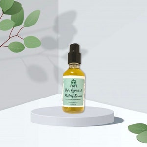 Puede incluir: Una botella de vidrio transparente con una boquilla de pulverización negra y una etiqueta verde. La etiqueta dice "Joli Hair Repair & Protect Serum".