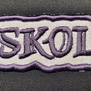 May include: Purple embroidered patch with the word "SKOL" in white lettering.