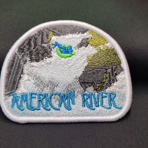 May include: White embroidered patch with a blue and green river scene and the text "AMERICAN RIVER" in blue.