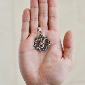 May include: Silver pendant featuring the Ukrainian trident symbol surrounded by a wreath of wheat.