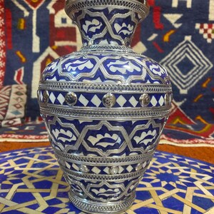May include: A blue and white ceramic vase with silver detailing. The vase has a geometric pattern and is decorated with silver studs.