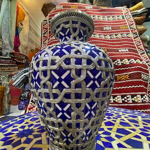 Peut inclure: Un vase en céramique bleu et blanc avec un motif en treillis métallique argenté. Le vase est posé sur une surface carrelée bleu et blanc.