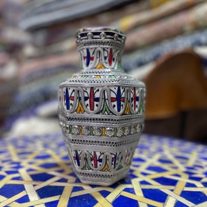 May include: A silver vase with intricate geometric patterns and colorful enamel accents. The vase is decorated with small, clear rhinestones.