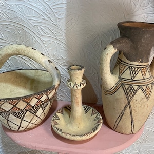 May include: Three ceramic pottery pieces with geometric patterns. A brown and white handled basket, a white candlestick, and a brown and white vase.
