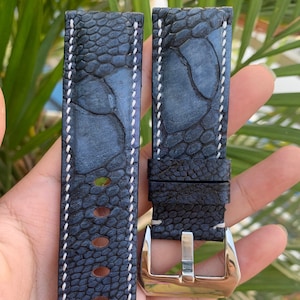 Puede incluir: Una correa de reloj de cuero azul oscuro con costuras blancas y una hebilla plateada. La correa tiene un patrón texturizado que se asemeja a escamas.