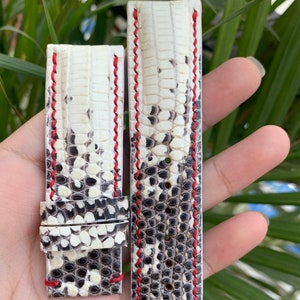 Puede incluir: Dos correas de reloj de cuero blanco con costuras rojas. Las correas están hechas de piel de serpiente y tienen un patrón texturizado.