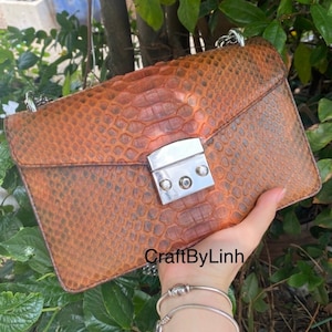 May include: A brown leather handbag with a snakeskin pattern and a silver clasp. The bag has a silver chain strap.