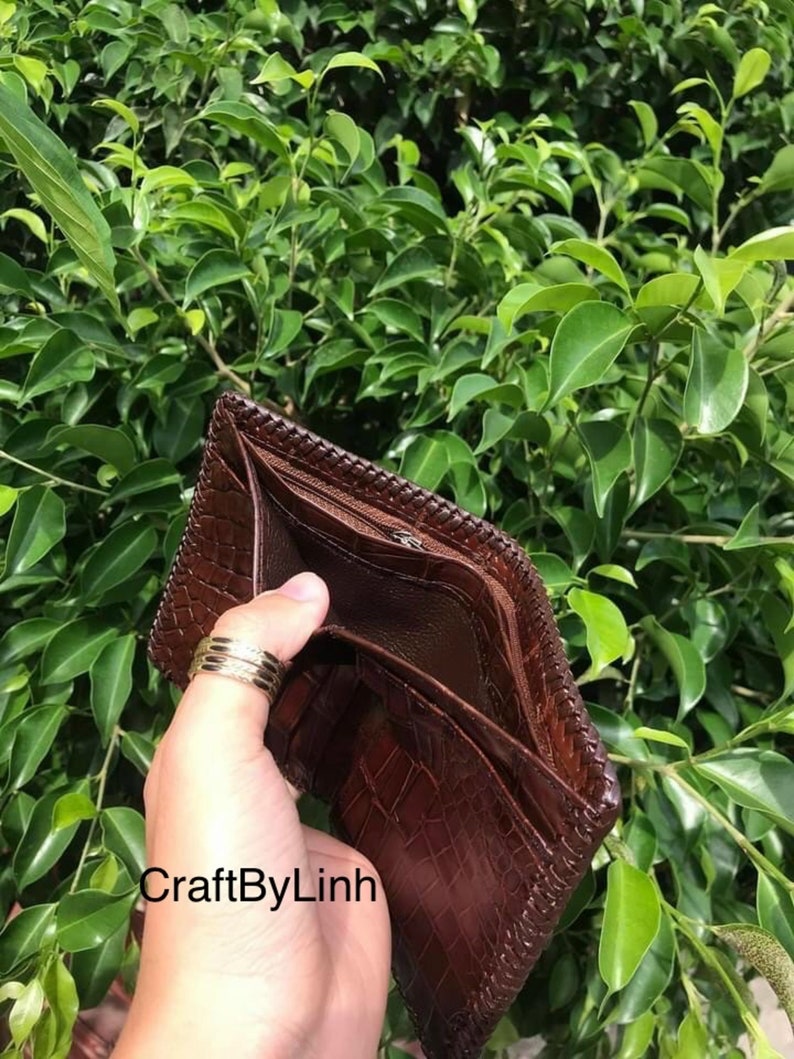 May include: A brown leather wallet with a crocodile pattern and a zipper closure. The wallet is open and empty, showing the interior lining. The text "CraftByLinh" is visible on the wallet.