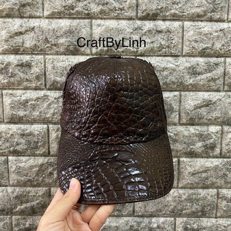 May include: A brown leather baseball cap with a crocodile skin pattern. The cap has a curved brim and an adjustable strap in the back.