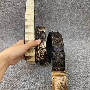 May include: Two crocodile leather belts with gold buckles. One belt is brown and the other is white. The buckle features a crocodile design.